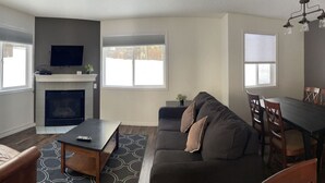 A living room with a fireplace, sofa, coffee table, TV, dining table, and chairs.