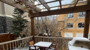 A covered patio with a grill, wooden chairs, and a table.