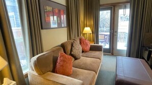 A hotel room with a sofa, a bed, a lamp, a small table, and a window with curtains.