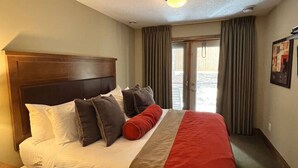 Ein Hotelzimmer mit einem großen Bett, einem Holzkopfende, einem roten Akzentkissen und Blick ins Freie durch eine Schiebetür.