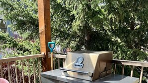 Ein tragbarer Gasgrill auf einem Balkon im Freien mit einem Stuhl und einem Holzgeländer.