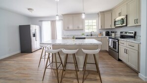 A modern kitchen with a central island, bar stools, stainless steel appliances, and light-colored cabinetry. - Charming 2-bedroom farmhouse in nice Wendell with AC, WiFi (Wendell)