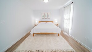 A bedroom with a bed, bedside lamps, a rug, and a window with curtains. - Charming 2-bedroom farmhouse in nice Wendell with AC, WiFi (Wendell)