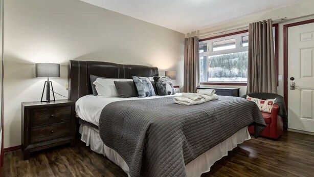 A bedroom with a bed, bedside table, lamp, window with curtains, and a door. - Yam 27/28 - Upper 2 Bedroom K/Q (Dead Man's Flats)