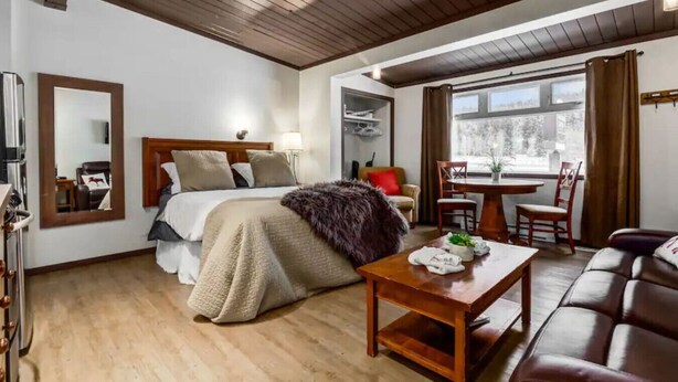 A hotel room with a bed, a wooden ceiling, a dining table with chairs, and a sofa.