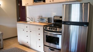 Una cucina compatta con mobili bianchi, un frigorifero in acciaio inossidabile, un forno a microonde, un tostapane e un forno.