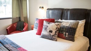 A bed with a quilt, a red chair, a nightstand, and a wall-mounted lamp. - Yam 12 - Studio with King (Dead Man's Flats)