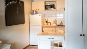 Eine kleine Küche mit weißen Schränken, einer Mikrowelle, einem Kühlschrank, einer Kaffeemaschine und einem Esstisch.