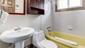 A bathroom with a white sink, toilet, and yellow bathtub. - Yam 23 - Upper Studio with King (Dead Man's Flats)