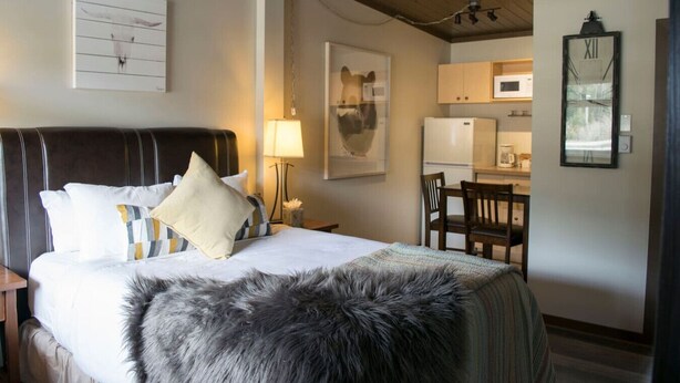 A hotel room with a bed, a desk, a chair, a lamp, a clock, and a framed picture on the wall. - Yam 23 - Upper Studio with King (Dead Man's Flats)