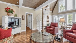 A spacious living room with a wooden ceiling, a glass coffee table, red leather sofas, and a television on a white cabinet.