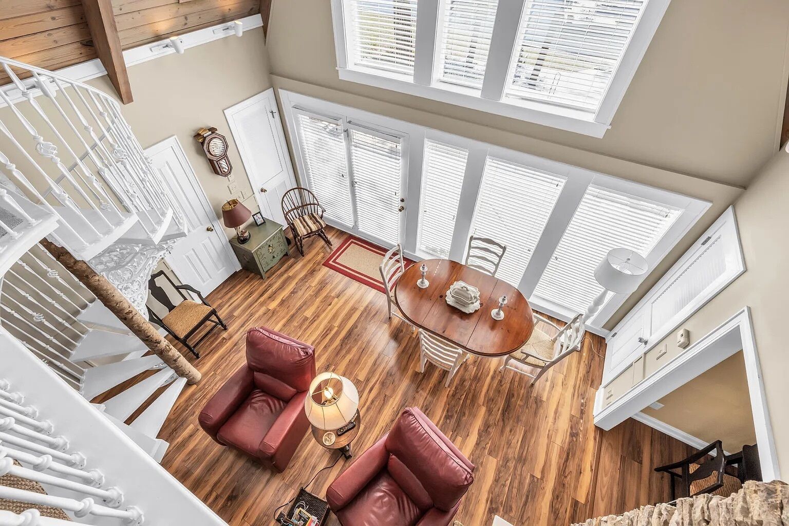 A spacious room with a wooden floor, a dining table with chairs, a red sofa, and a large window with blinds.
