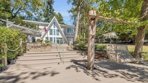 A wooden staircase leading to a building with a triangular roof, surrounded by trees and a bench.