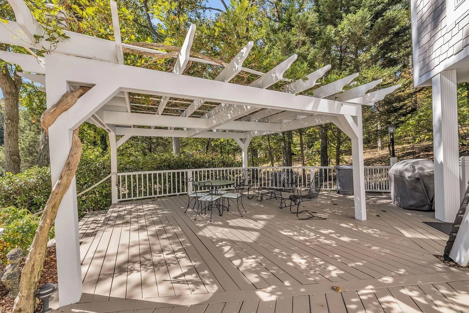 A covered outdoor deck with a pergola, picnic tables, and a barbecue grill.