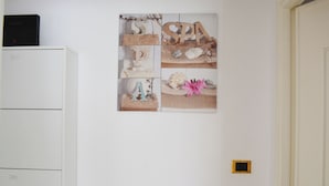 Een muur met een fotocollage, een wit kastje en een deur.
