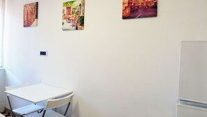 Een kamer met een witte tafel en stoelen, drie ingelijste foto's aan de muur en een witte koelkast.