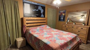 Ein Schlafzimmer mit einem hölzernen Bett, einem Deckenventilator, einer Karte an der Wand und einer Kommode mit Spiegel.