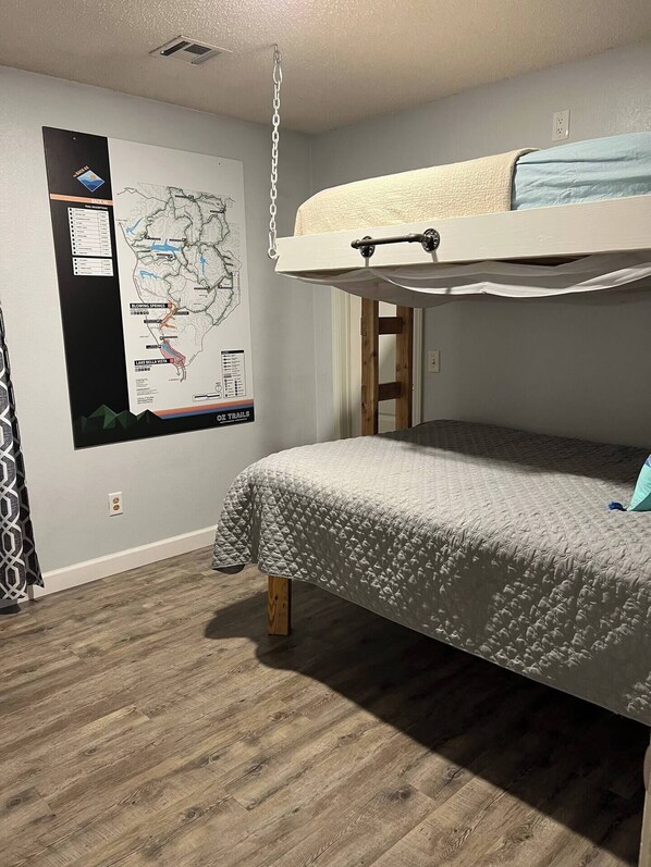 Une chambre avec un lit superposé, une carte accrochée au mur et un plancher en bois.