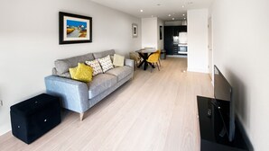 A modern living room with a grey sofa, yellow cushions, a dining table with yellow chairs, and a black TV stand. - Argyle Street - Apartment 2 (Glasgow)