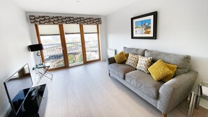 A modern living room with a grey sofa, yellow cushions, a framed picture on the wall, and a large window with blinds. - Argyle Street - Apartment 2 (Glasgow)