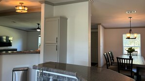 A modern kitchen with a granite countertop, stainless steel sink, and a built-in oven. There is a dining area with a table and chairs visible in the background.