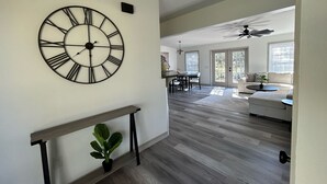 A spacious living area with a large wall clock, a dining area, and a seating area with a ceiling fan.