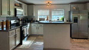 A modern kitchen with white cabinets, a central island, stainless steel appliances, and a farmhouse sign.