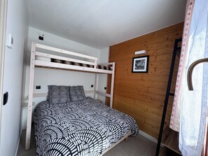 Un letto a castello con copriletto fantasia, una parete in legno, un quadro incorniciato e una tenda.