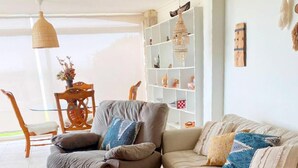 Un soggiorno con divano, poltrona e tavolino. Si nota una libreria con oggetti decorativi e una lampada a sospensione.