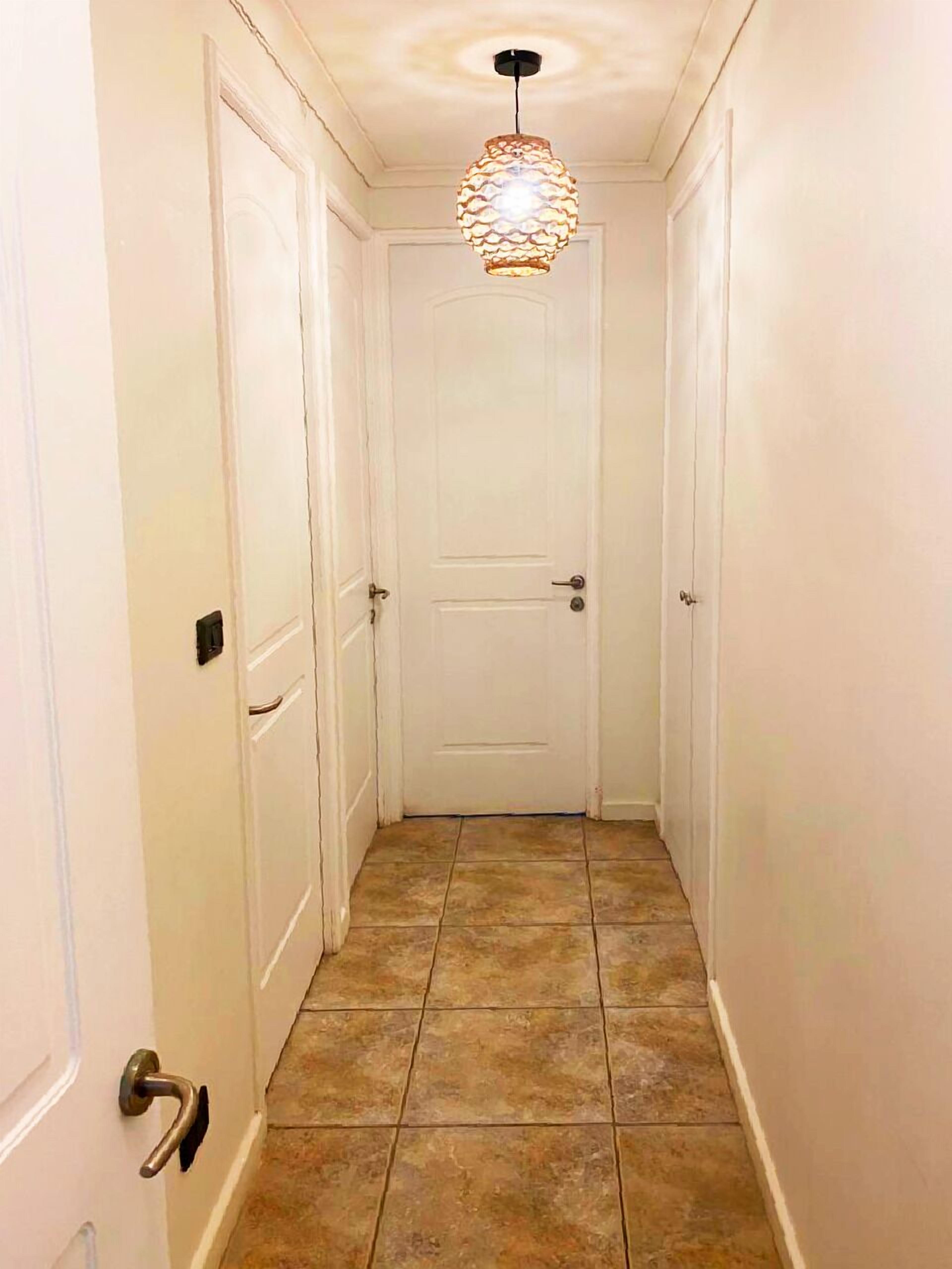 A narrow hallway with white doors and a tiled floor.