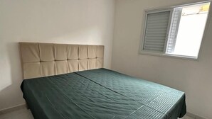A bedroom with a bed, a window, and a light-colored tiled floor. - CASA DA ALEGRIA (Praia Grande)