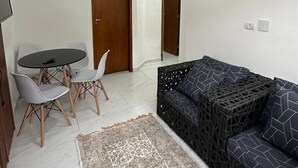 A living room with a sofa, a dining table with chairs, a painting on the wall, and a ceiling light. - CASA DA ALEGRIA (Praia Grande)