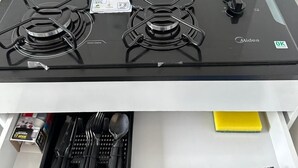 A kitchen with a gas stove, four burners, and a range hood. Below the stove, there is a utensil holder with various kitchen tools. - CASA DA ALEGRIA (Praia Grande)