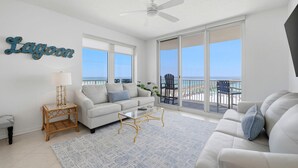A spacious living room with a white sofa, a coffee table, and a large window with a view of the beach. - Inn At Summerwind 501 - This Is It (Navarre)
