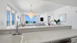 A modern kitchen with a large island, a chandelier, and a view of the ocean. - Inn At Summerwind 501 - This Is It (Navarre)