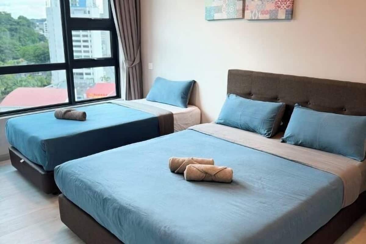 A hotel room with two beds, each with blue bedding and pillows, and a large window offering a city view.