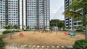A playground with sand, swings, and a climbing structure, surrounded by a stone wall and palm trees, with tall buildings in the background. - JQ#11 City View Slide LoftBed 2R1B 5Pax Near Suria Mall, Gaya St, Sicc (Kota Kinabalu)
