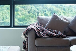 Un sofá con una manta y almohadas, una ventana con vistas a la vegetación y una parte de una cama.