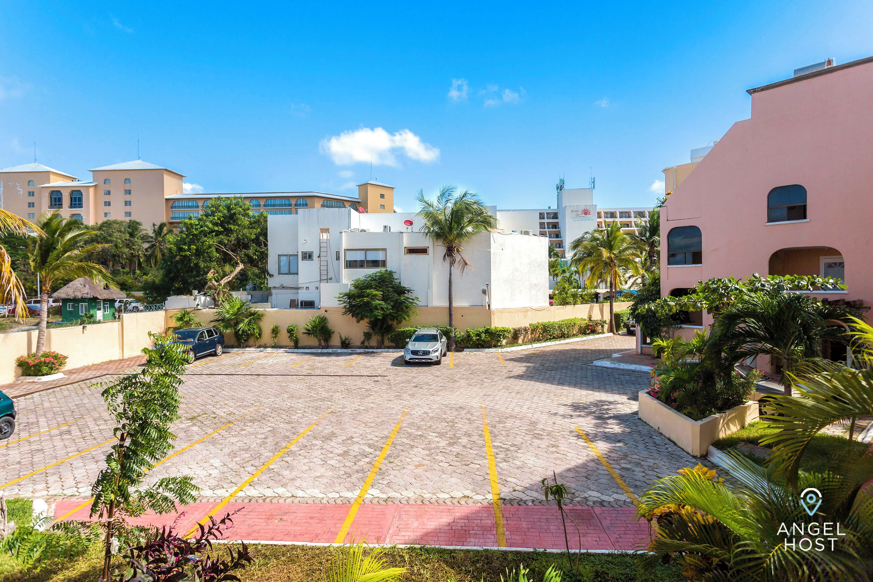 A parking area with a white car, surrounded by buildings with balconies and palm trees.