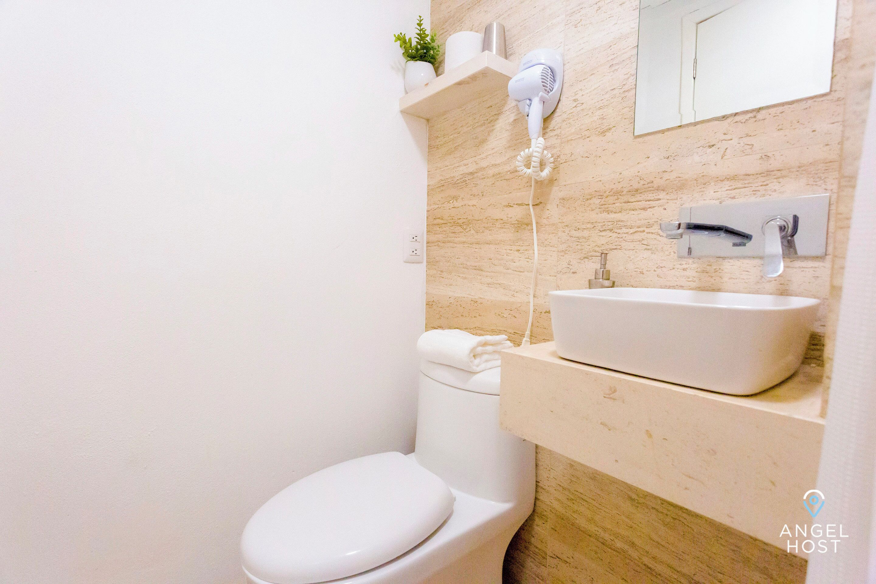 Ein modernes Badezimmer mit Toilette, Waschbecken und Wandhaartrockner, alles in Weiß.