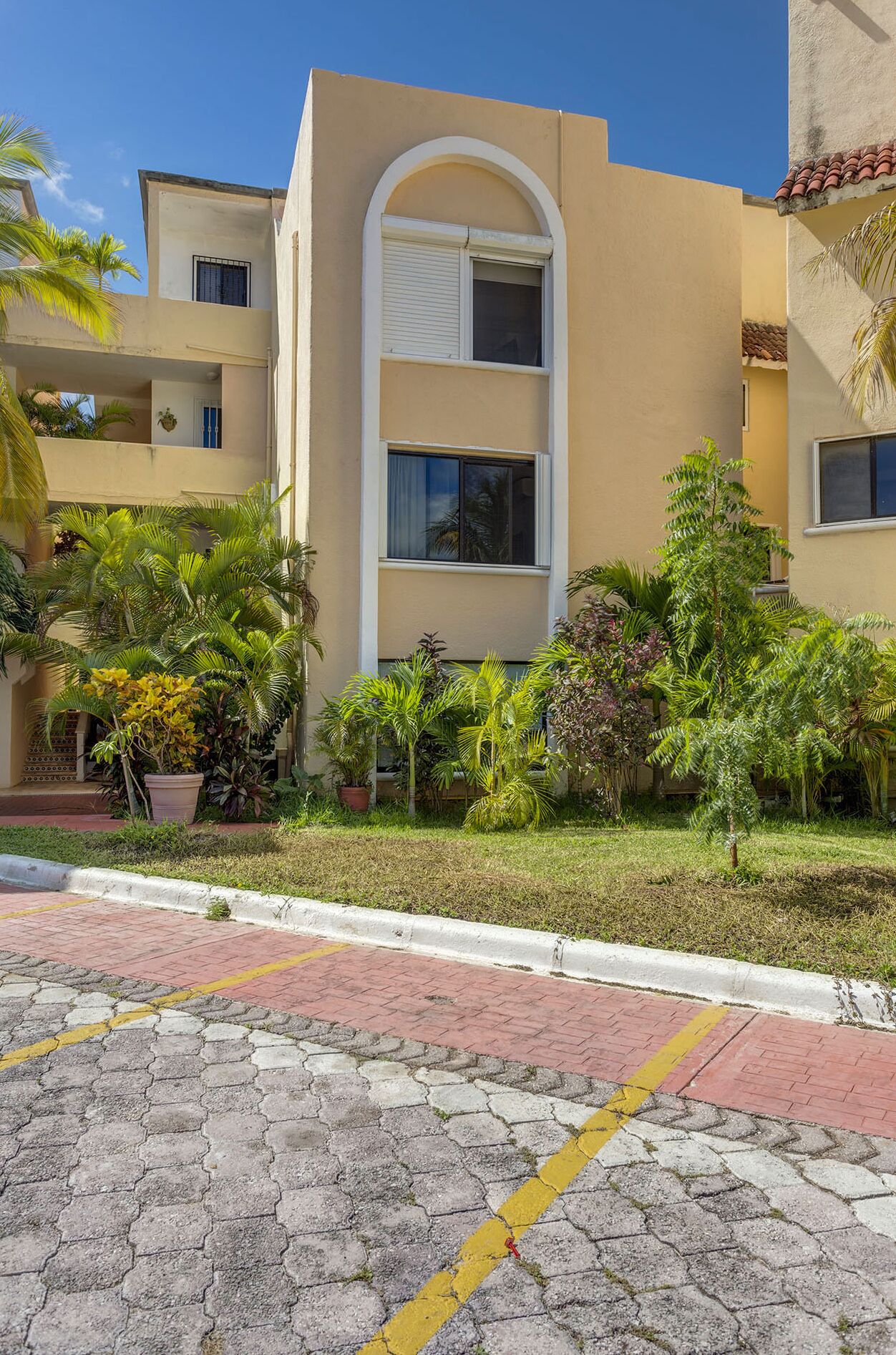 A multi-story building with a flat roof, surrounded by lush greenery and a paved walkway.