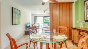 Zona pranzo con tavolo in vetro, sedie di legno e ventilatore a soffitto.