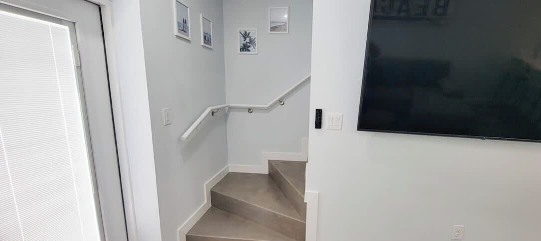 A staircase with a handrail, a door, and a wall with a mounted television.