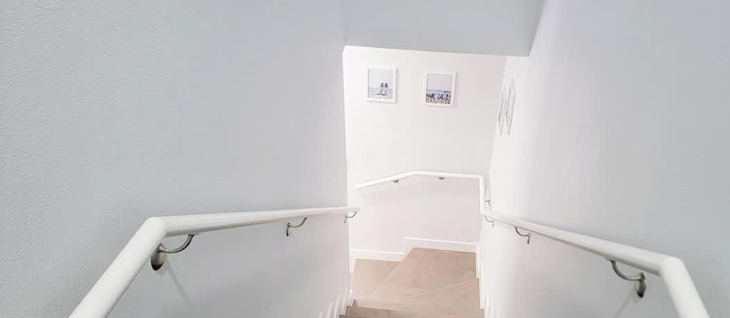 A staircase with white walls and handrails, leading to a landing with two framed pictures.