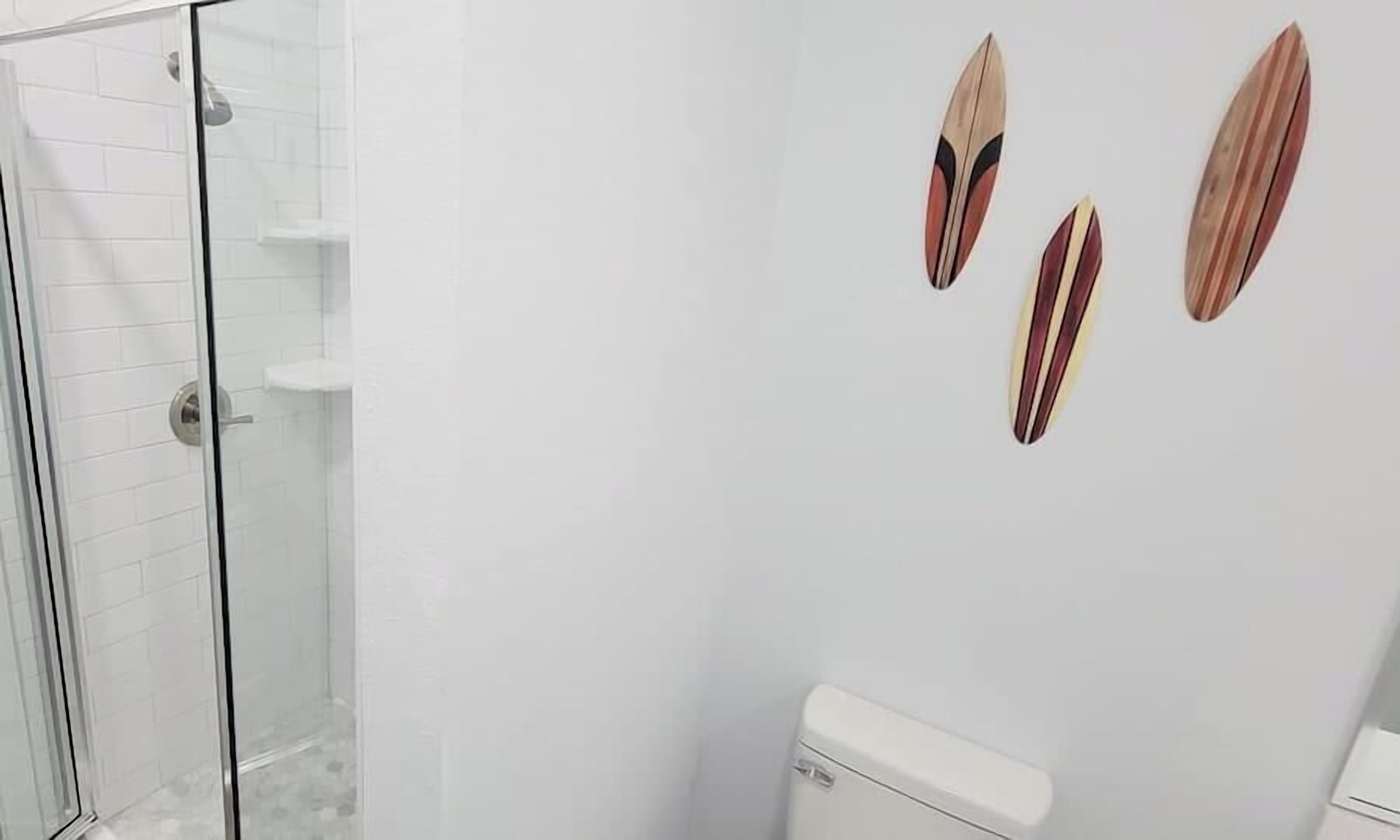 Une salle de bain avec une douche à parois de verre, des toilettes blanches et trois éléments de décoration en bois fixés au mur.