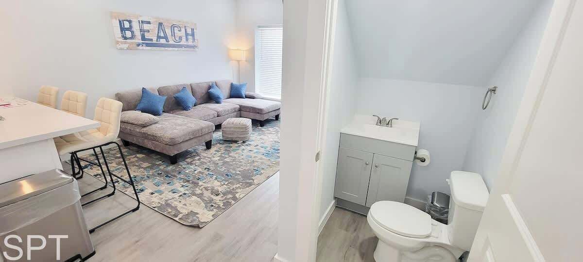 Un salon avec un canapé, des fauteuils et un tapis. Il y a une salle de bain avec des toilettes, un lavabo et des placards.