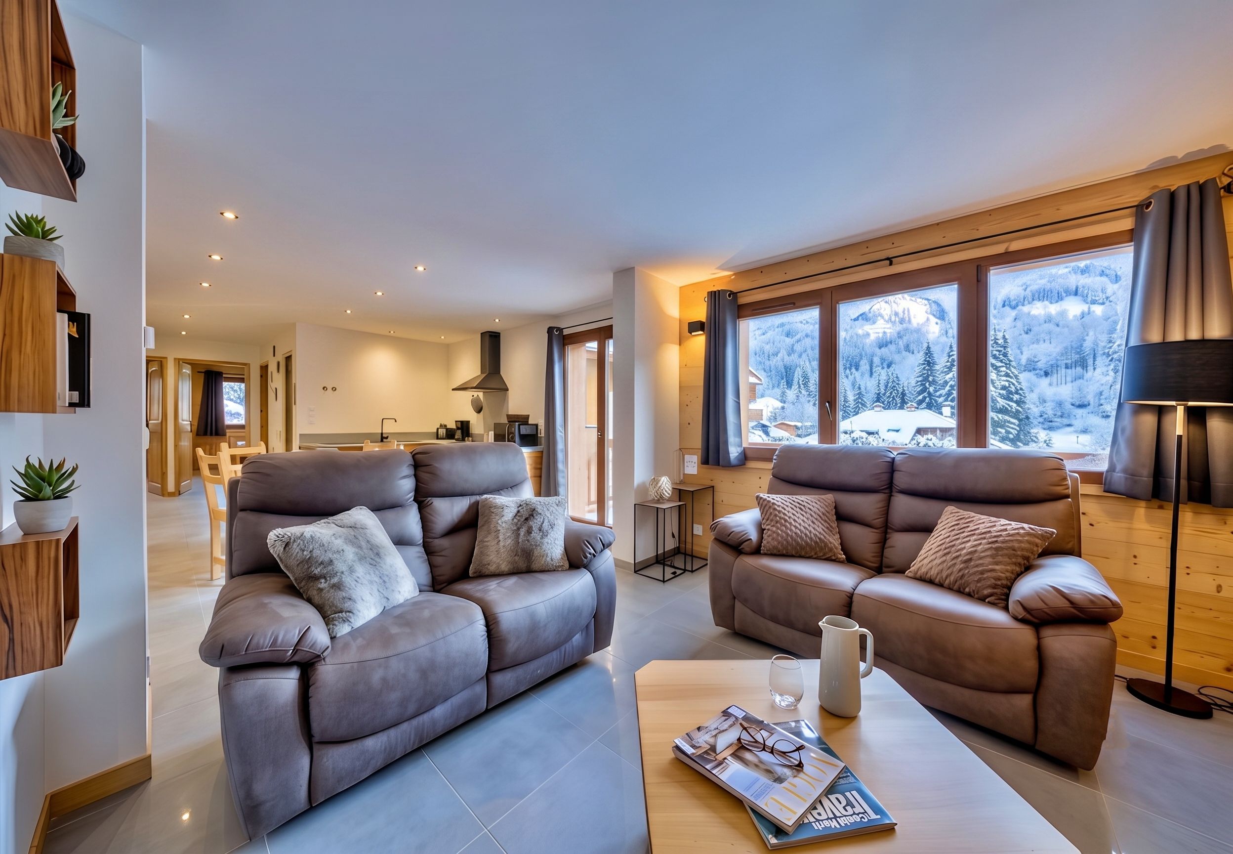 Ein modernes Wohnzimmer mit zwei Sofas, einem Couchtisch und einer Zeitschrift. Fenster bieten Blick auf einen verschneiten Berg.