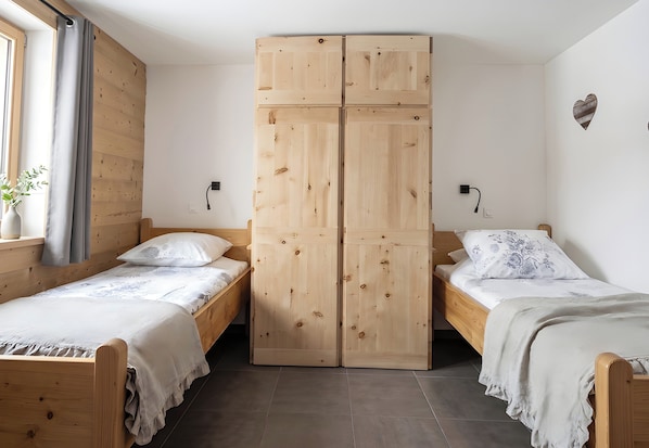 A room with two wooden beds, a wardrobe, and a window with curtains. - CASA-Mezan, appartement cosy 2 chambres (Aiguilles)