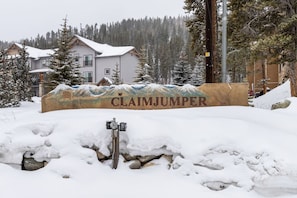 Segnaletica innevata con il nome "CLAIMJUMPER" di fronte a un edificio con facciata in legno e montagne sullo sfondo.