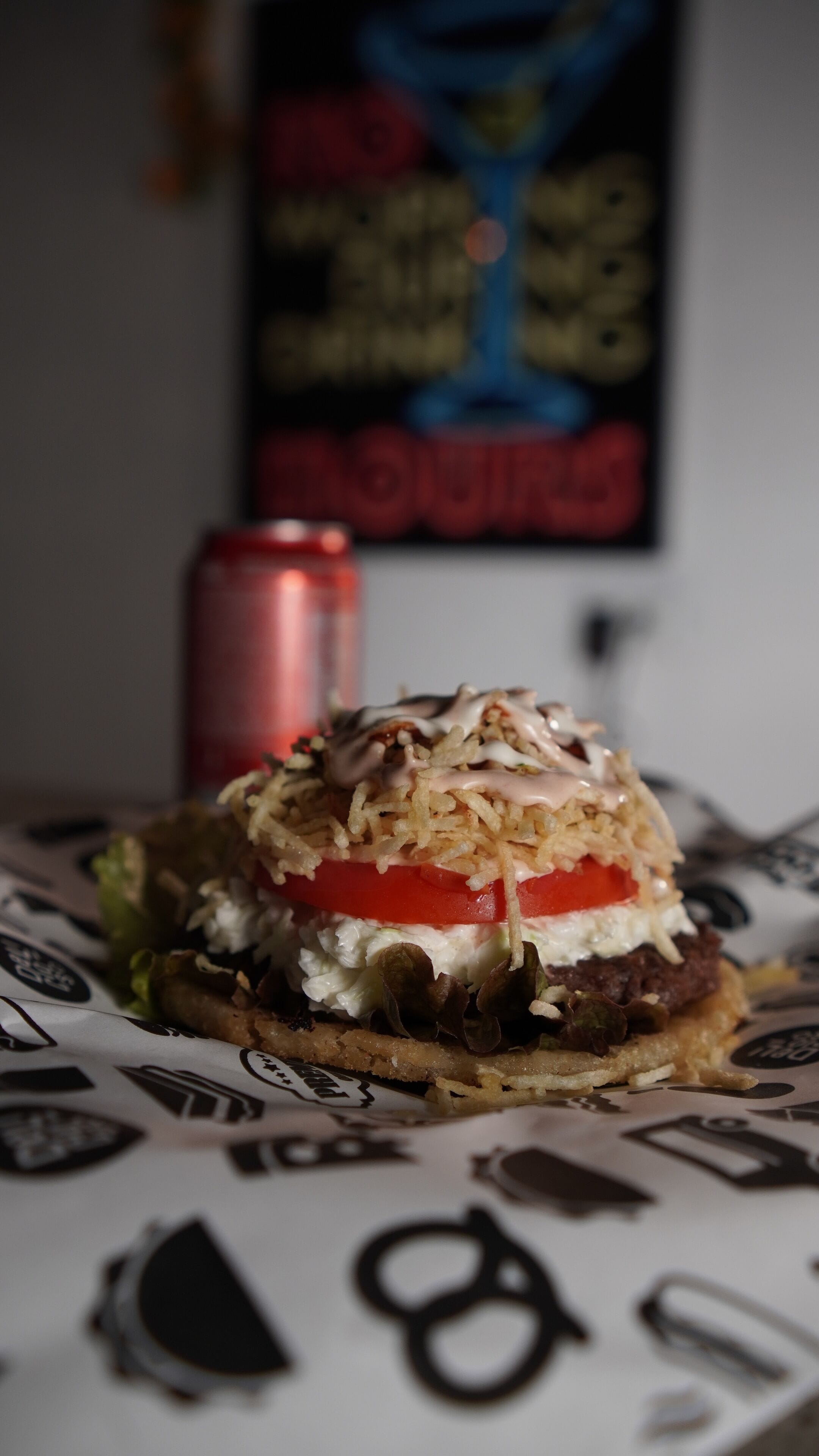 Una hamburguesa con una rodaja de tomate, lechuga y salsa, sobre un papel con un logotipo.
